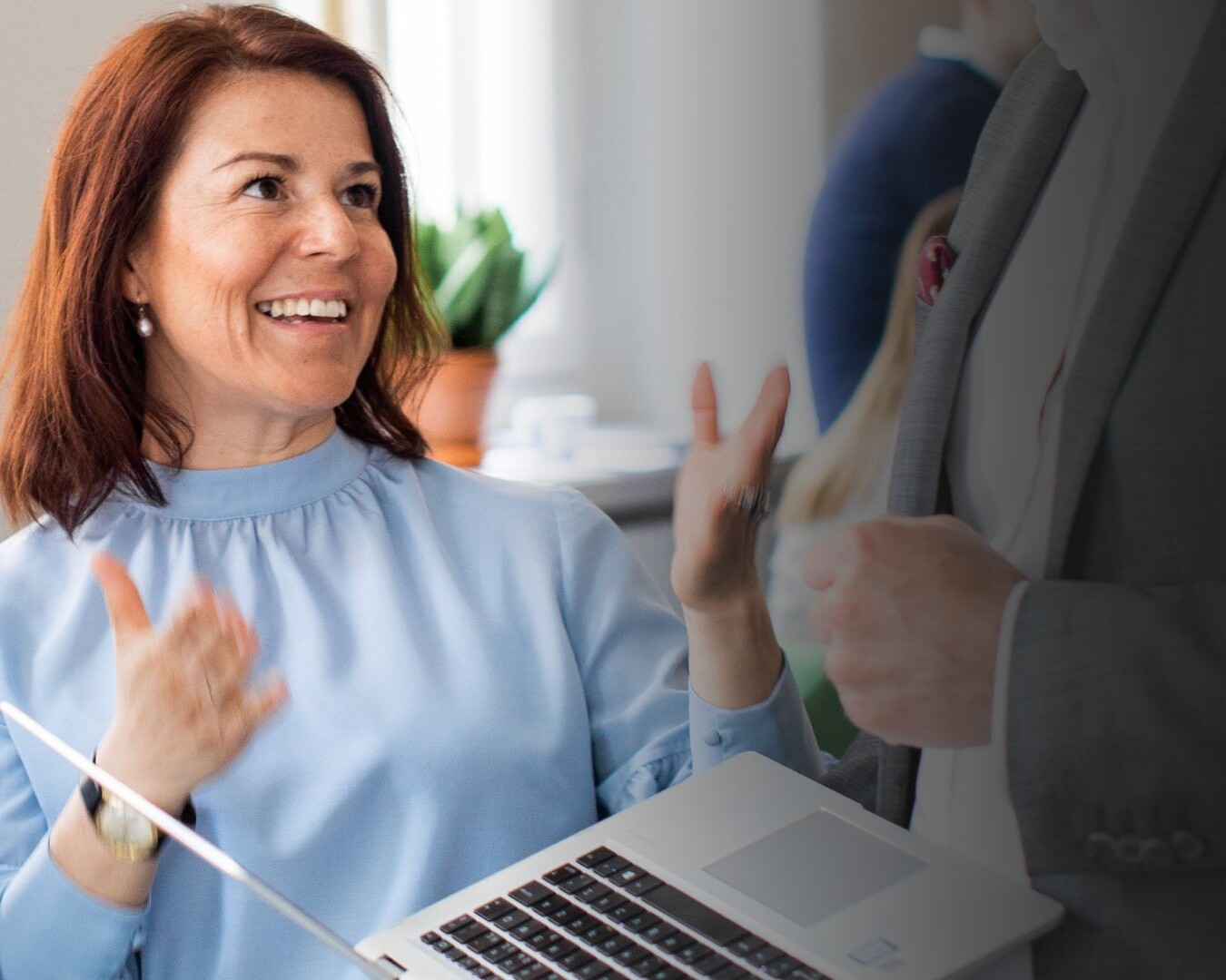 Paula i blå blus ler mot kollega med dator i handen
